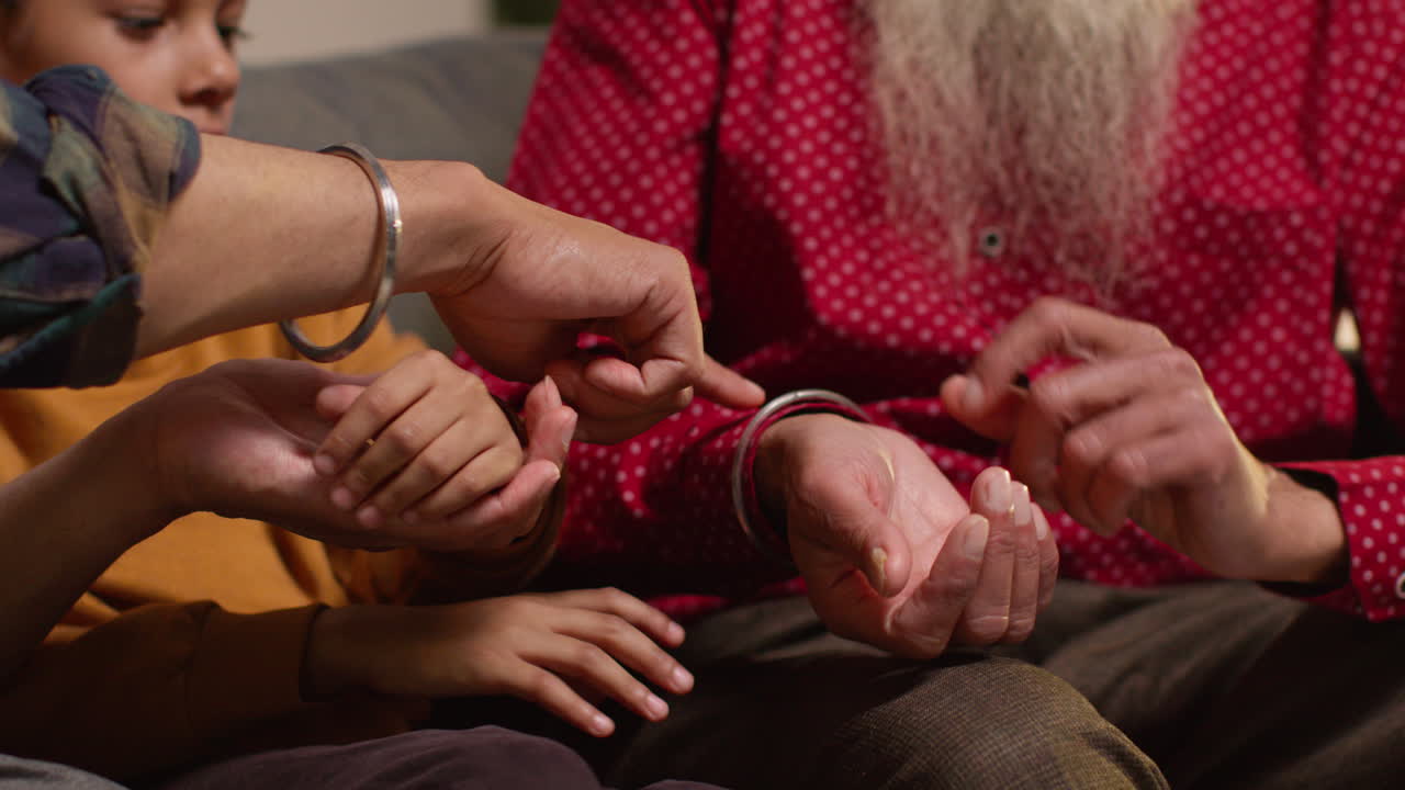 primer plano de una familia sikh masculina de varias generaciones usando y discutiendo brazaletes o pulseras tradicionales de plata sentados en el sofá en casa 3
