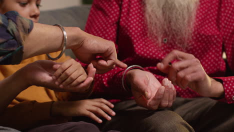 primer plano de una familia sikh masculina de varias generaciones usando y discutiendo brazaletes o pulseras tradicionales de plata sentados en el sofá en casa 3