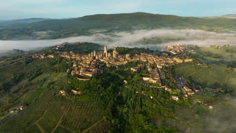 panoramic view over san gimignano town with fog over the hills in tuscany, italy - aerial drone shot