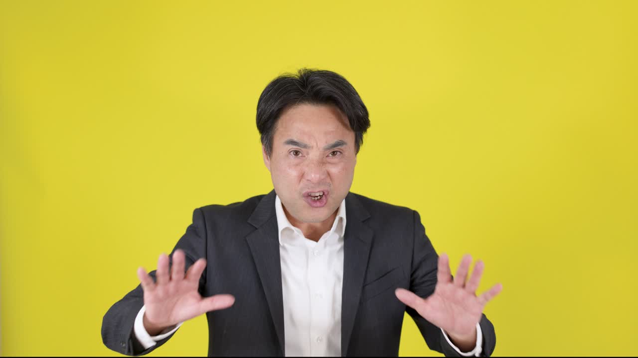 スーツを着た男性が警告するように手を上げ、深刻な表情、黄色い背景、スタジオ照明。
