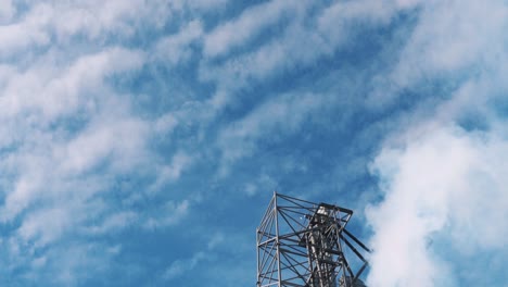white smoke from a factory against a blue sky with clouds. metal structures of the plant. industrial zone