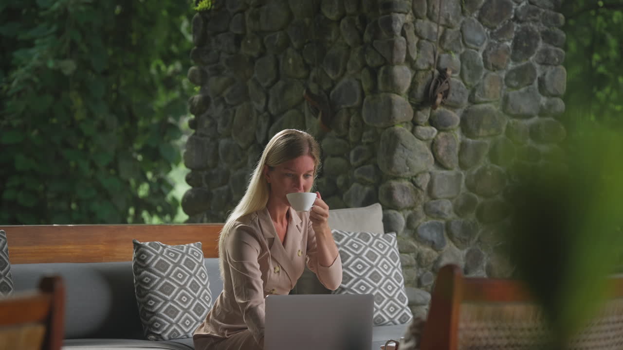 Focused business woman working on laptop at Bali resort lounge while drinking coffee