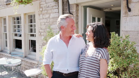 Happy-mature-couple-stand-embracing-outside-their-restaurant-pub-business