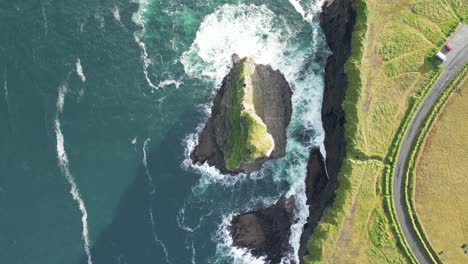 aerial view of a rugged coastline with waves crashing on rocks, greenery nearby