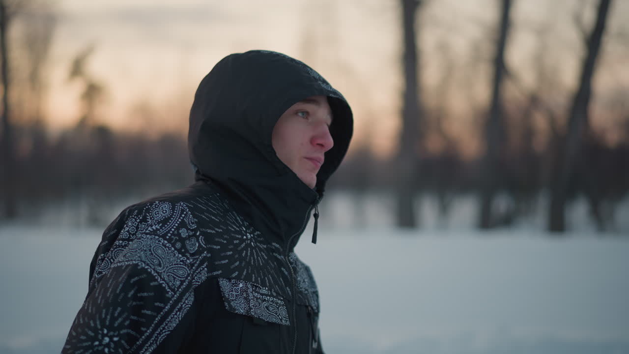 close up of white man in hoodie gliding on ice under soft sunset light winter park blur background motion focus on face and hooded jacket coat zipped warmly visible breath mist steam