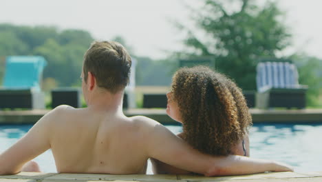 rear view of loving couple relaxing in swimming pool on vacation celebrating drinking champagne