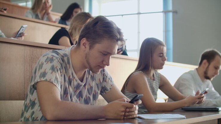 A group of men and women in a large university audience silently look at the screens of smartphones and write chat messages. Each person looks at the screens of his device without paying attention to the events of the real world.