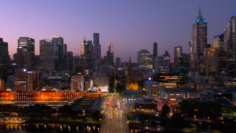 dramatic dusk view of melbourne looking directly down elizabeth street with flinders street station and fed square illuminated against the night sky
