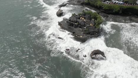 Aerial:-Ocean-waves-smash-onto-rocky-islet-of-Tanah-Lot-temple,-Bali