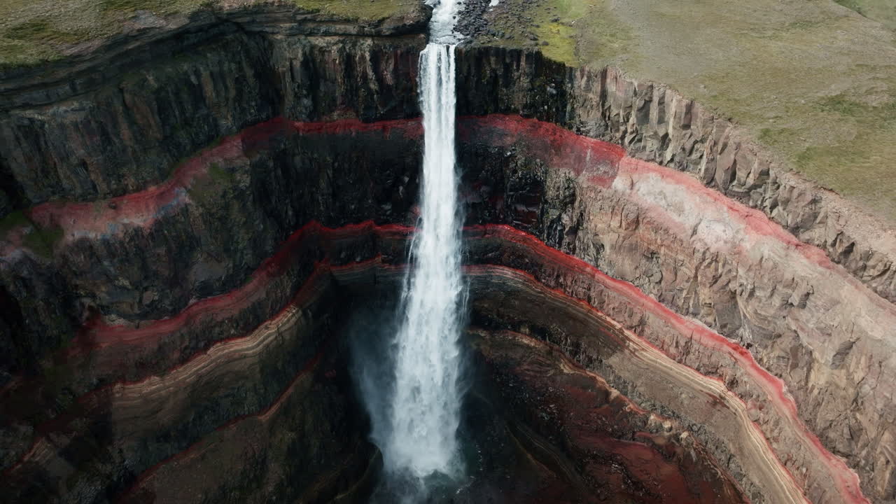Close up aerial drone shot of Hengifoss Waterfall in motion, Iceland, sunny day, green grass, red clay. Part 6.