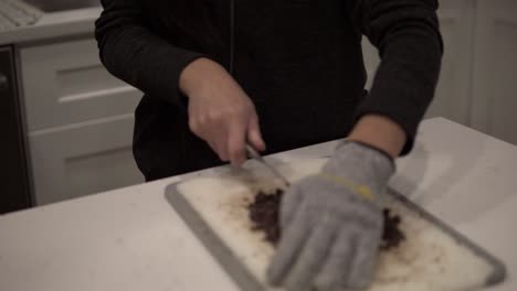 a young korean girl cuts up dark chocolate before melting it for millionaire shortbread cookies while wearing safety gloves-1