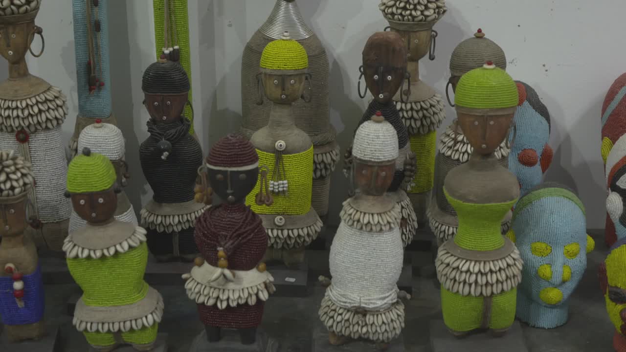 Close-up shot of artistic handmade figurines representing Gnaoua musicians. The dolls feature traditional colorful attire and hats adorned with cowrie shells, displayed in a shop in Essaouira