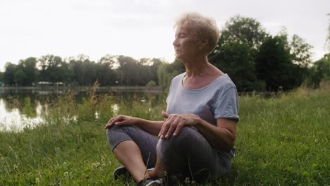 Mujer-Mayor-Tranquila-Meditando-En-El-Parque-Junto-Al-Lago