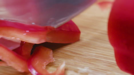 slow motion - detail shot of a knive cutting and slicing a red paprika on a wooden board