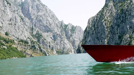 albania, lago koman, proa de un barco rojo en la superficie del lago, con las montañas malditas en el fondo