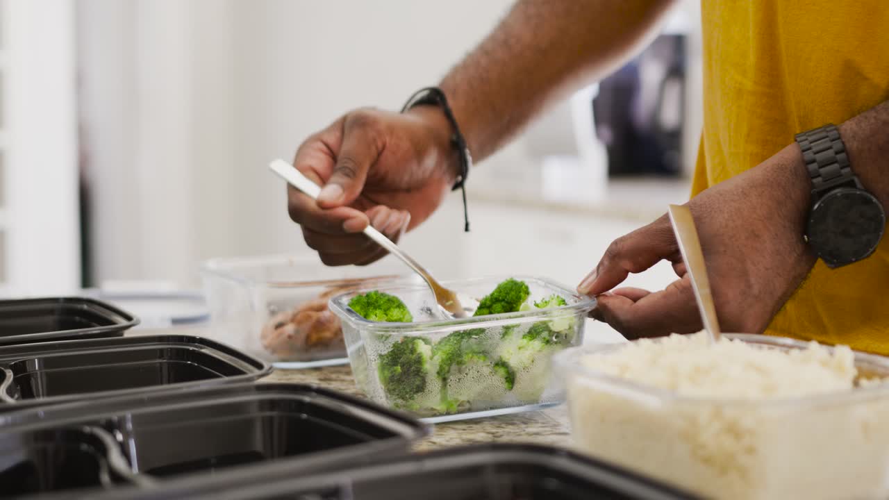 Nach dem Kochen füllt ein Mann in gelbem Hemd Brokkoli in Meal-Prep-Behälter auf der Arbeitsplatte, mit Freiraum für Text.