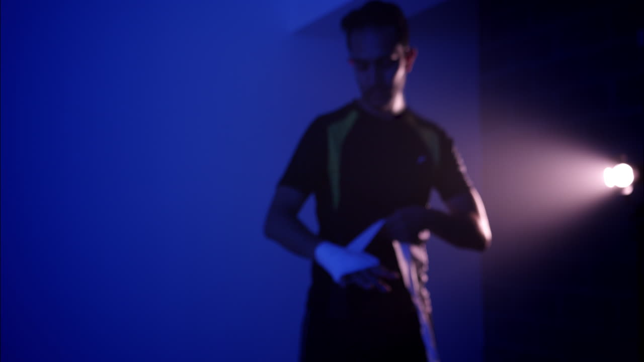 Uomo che si fascia le mani con le fasce da boxe in una palestra buia.