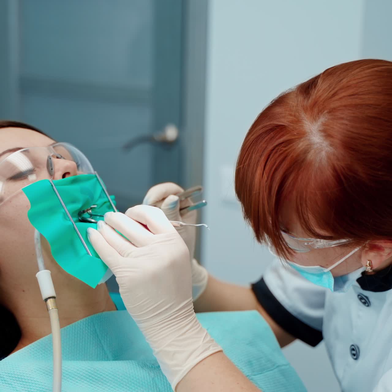 Orthodontic procedure. Female patient in safety goggles sitting in dental chair during tooth treatment. Professional stomatologist treats woman's teeth in dental office.