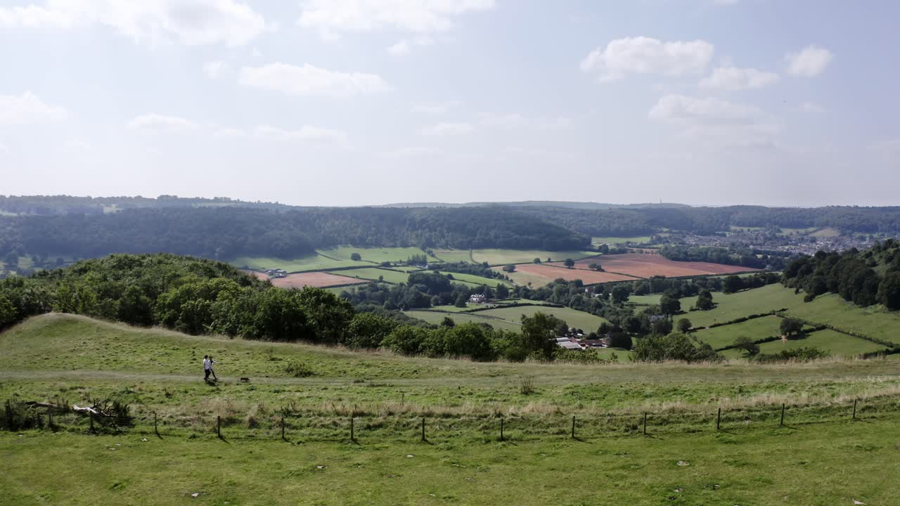 AEREA - Coppia porta a spasso il cane su una collina vicino a Uley, Cotswolds, Inghilterra, inquadratura ampia statica