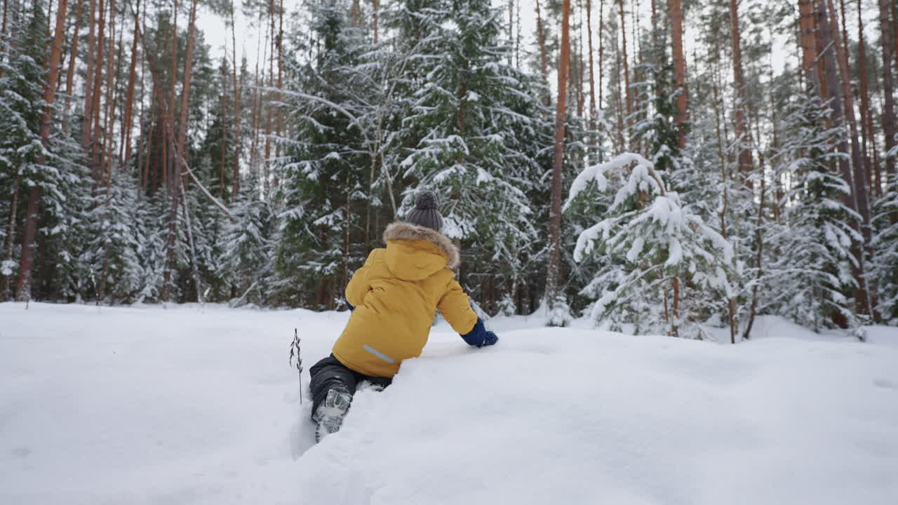 un niño con una chaqueta amarilla camina a través de la nieve profunda estudiando los paseos invernales del bosque invernal y a través del bosque nevado en cámara lenta. el concepto de un entorno libre para los niños