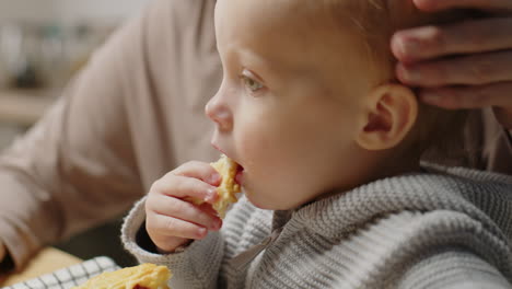 baby eating puff pastry at kitchen table with loving mom