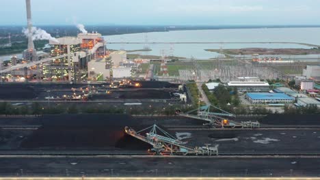 tracking shot across coalfield and industrial ultra-supercritical coal-fired power plant with smokes raising from chimney located at lekir bulk terminal jalan, teluk rubiah, manjung, perak, malaysia