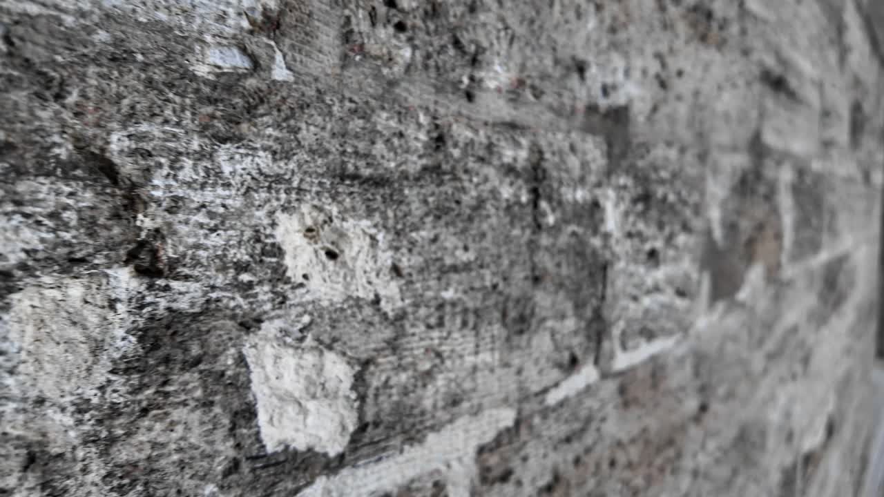 Panoramica lenta su un muro di mattoni grigi, texturizzato e consumato.