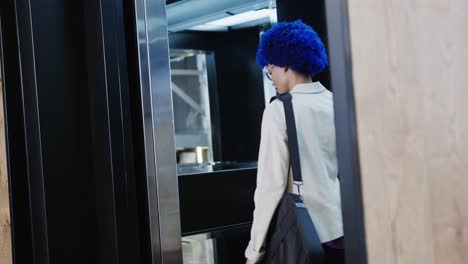 mujer de negocios biracial con afro azul hablando en teléfono inteligente y usando ascensor, cámara lenta