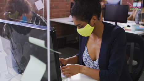 mixed race businesswoman having video chat sitting in front of computer wearing face mask