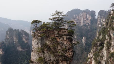A lone sandstone pillar crowned with pine trees rises dramatically above the forested canyon in the Zhangjiajie National Forest Park.