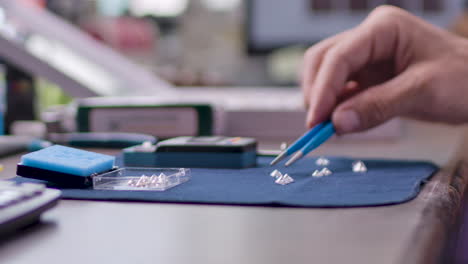 male hand sorting round cut polished diamonds on the table with tweezers