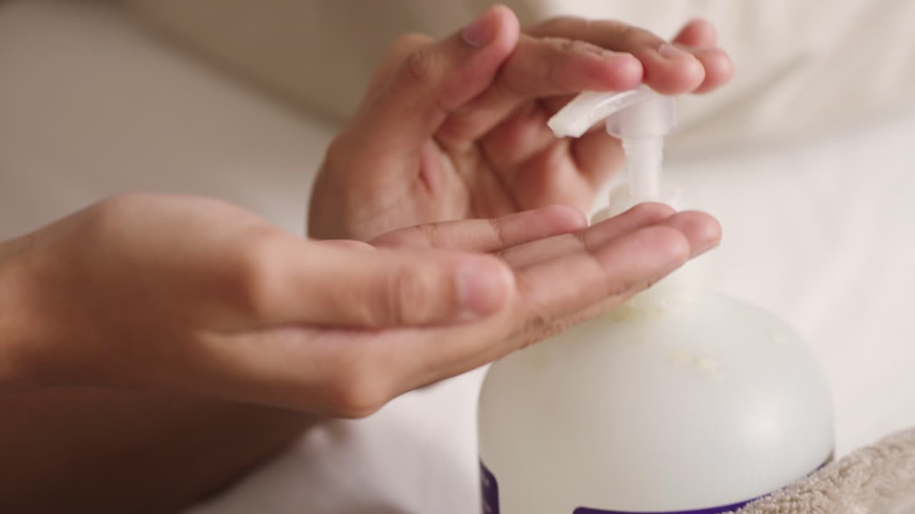 Manos jóvenes morenas bombeando loción de una botella a las manos