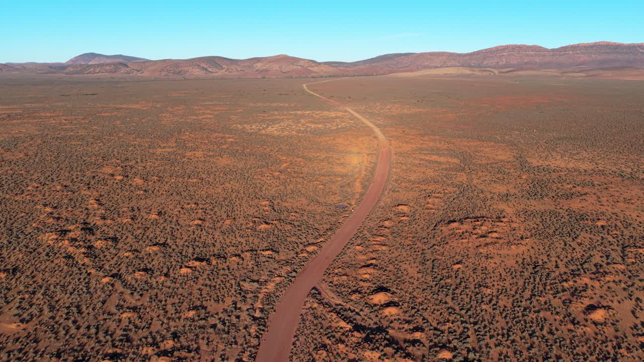 Long dirt road stretching through arid outback landscape towards Flinders Ranges mountains in golden light
