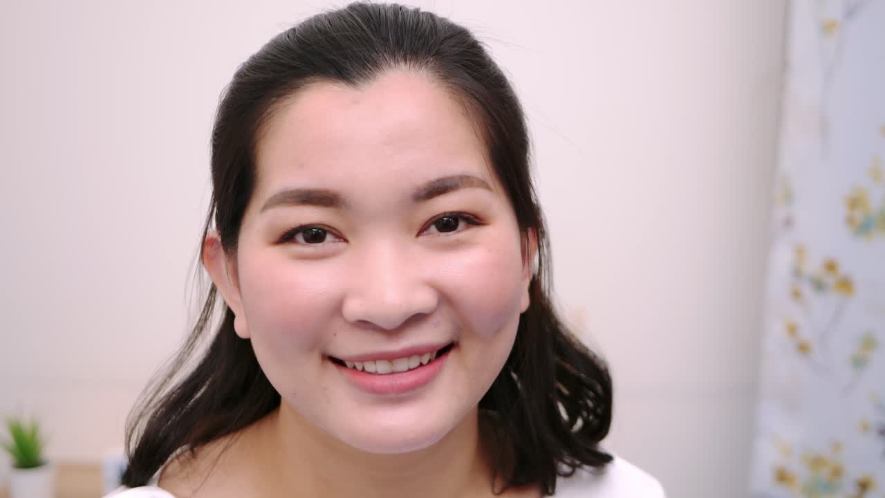 아름답고 웃고 있는 아시아 여성들은 휴일에 혼자 전문적인 초상화를 취한 카메라를 바라보며 극도로 자신감 있는 젊은 얼굴을 하고 맑은 빛, 슬로우 모션 장면으로 휴식을 취합니다.