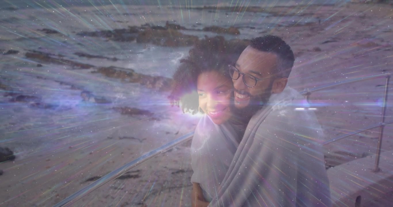 Pareja envolviéndose en una manta en el paseo marítimo para un anuncio de estilo de vida, causando un destello de lente animado con luz brillante.