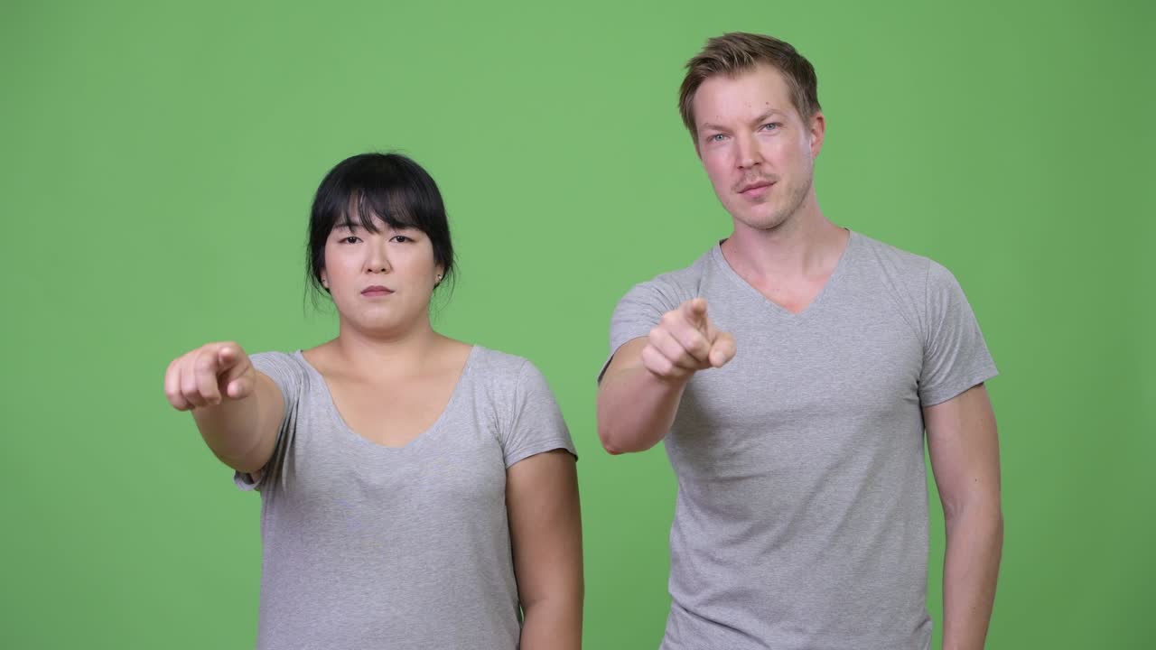 Young multi-ethnic couple pointing at camera together