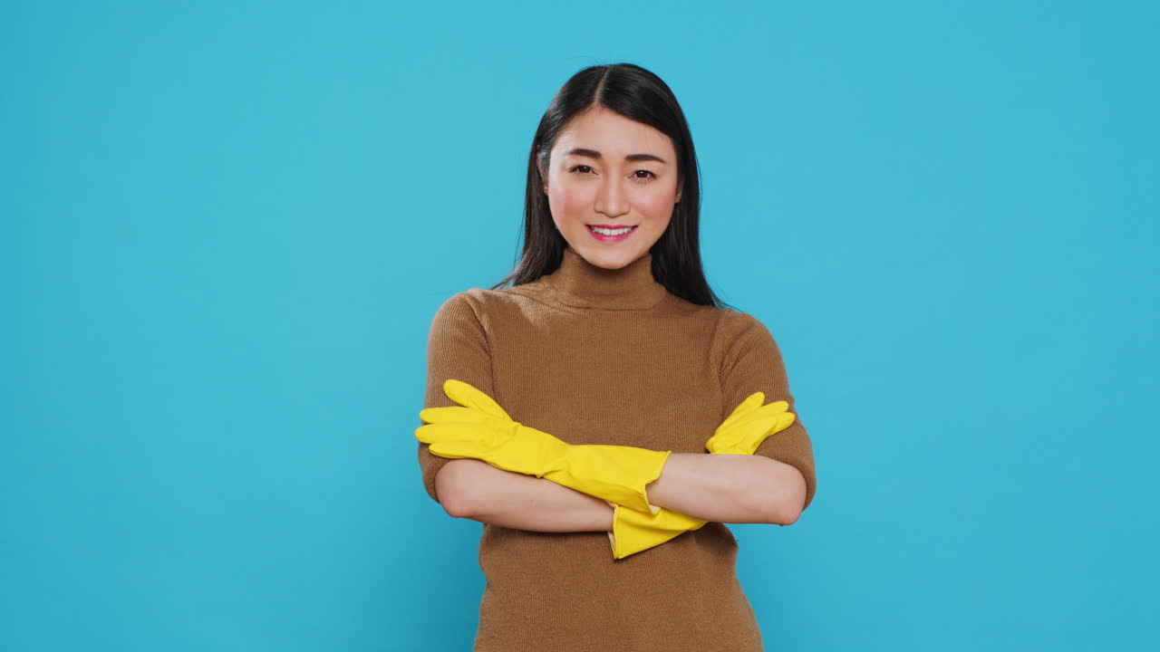 Smiling professional maid wearing protective rubber gloves standing with arm crossed in studio
