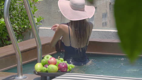 a woman in a black bathing suit and a straw hat on her head enjoys in a private swimming pool with a beautiful view of the city