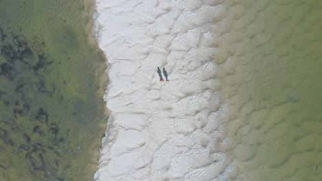 aerial vertical view of a couple walking through out a sand bank with water on both sides