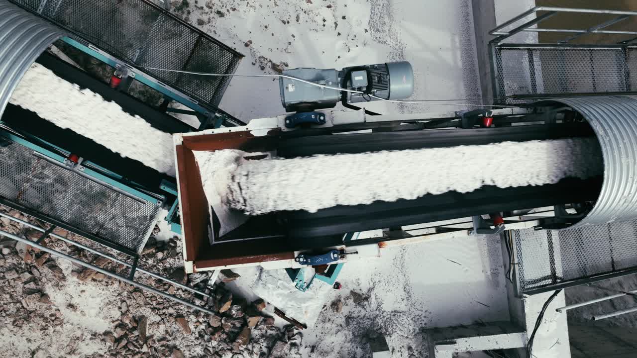 A high-angle view of a conveyor belt transporting crushed material at an industrial site. Moving material as part of a large-scale mining or quarrying process