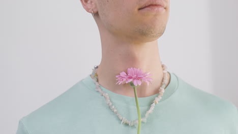 close up young man with necklace and t shirt holding a flower 1