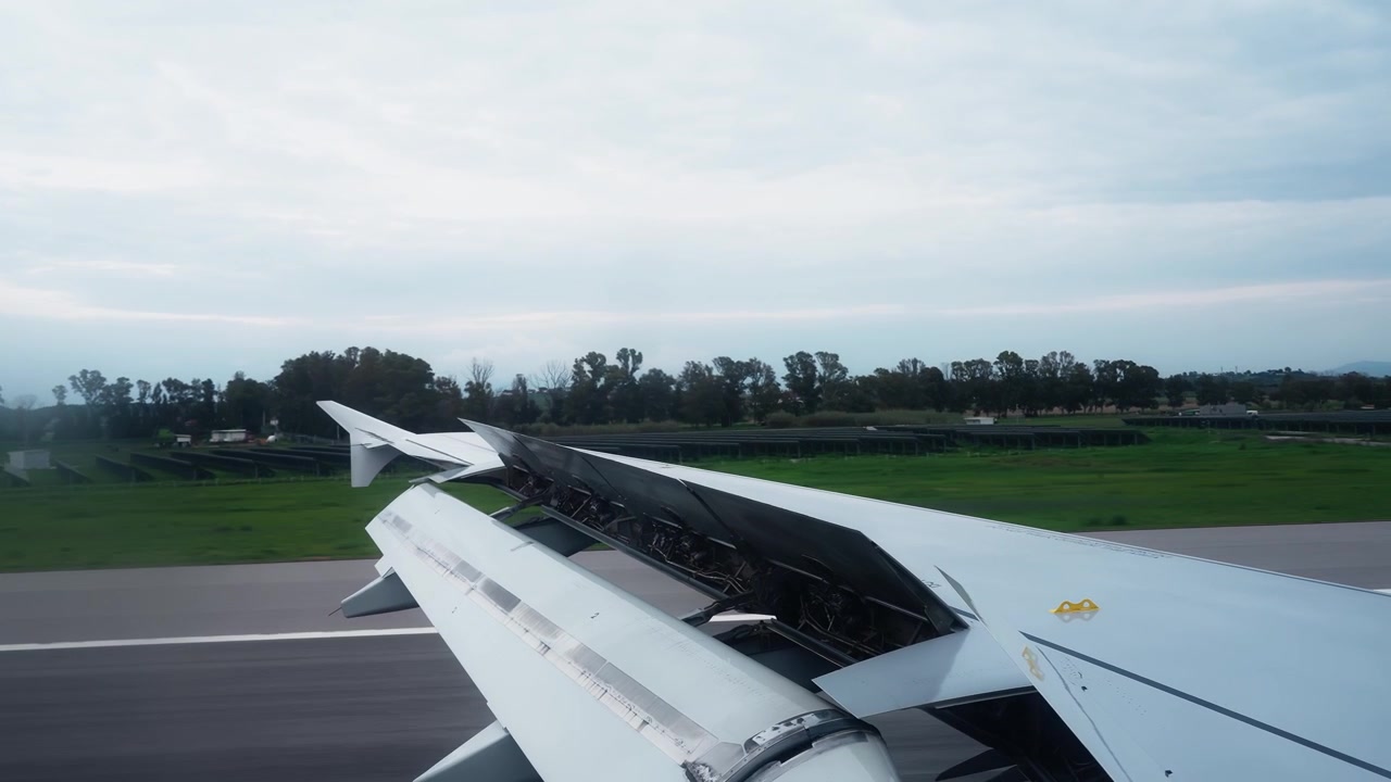 Vista desde la ventanilla del pasajero de un ala de avión rodando por la pista después de aterrizar, con los flaps extendidos, un aeródromo verde al fondo y un cielo nublado y tranquilo.