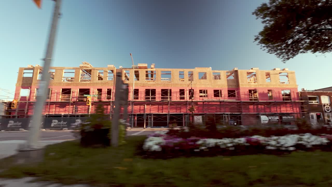 Side view from car driving past historic red and white buildings; trees in foreground; blue fall sky