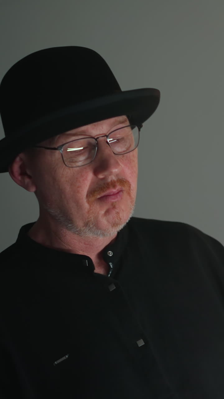 tecladista enfocado en sombrero negro y traje juega un sampler rojo en un estudio gris de mal humor