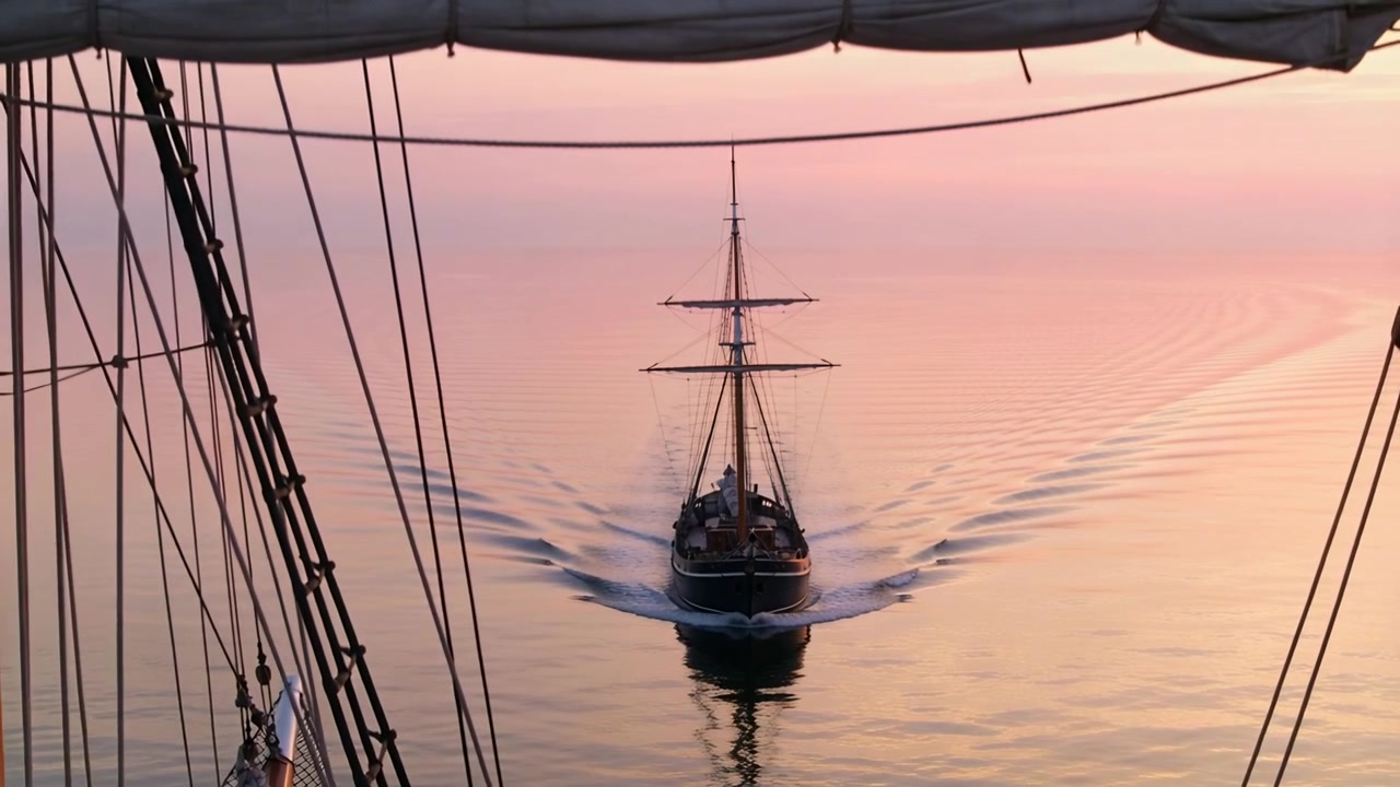 Una nave a tre alberi che si avvicina, mantenendo la rotta verso il ponte all'alba, incorniciata dal sartiame del boma.