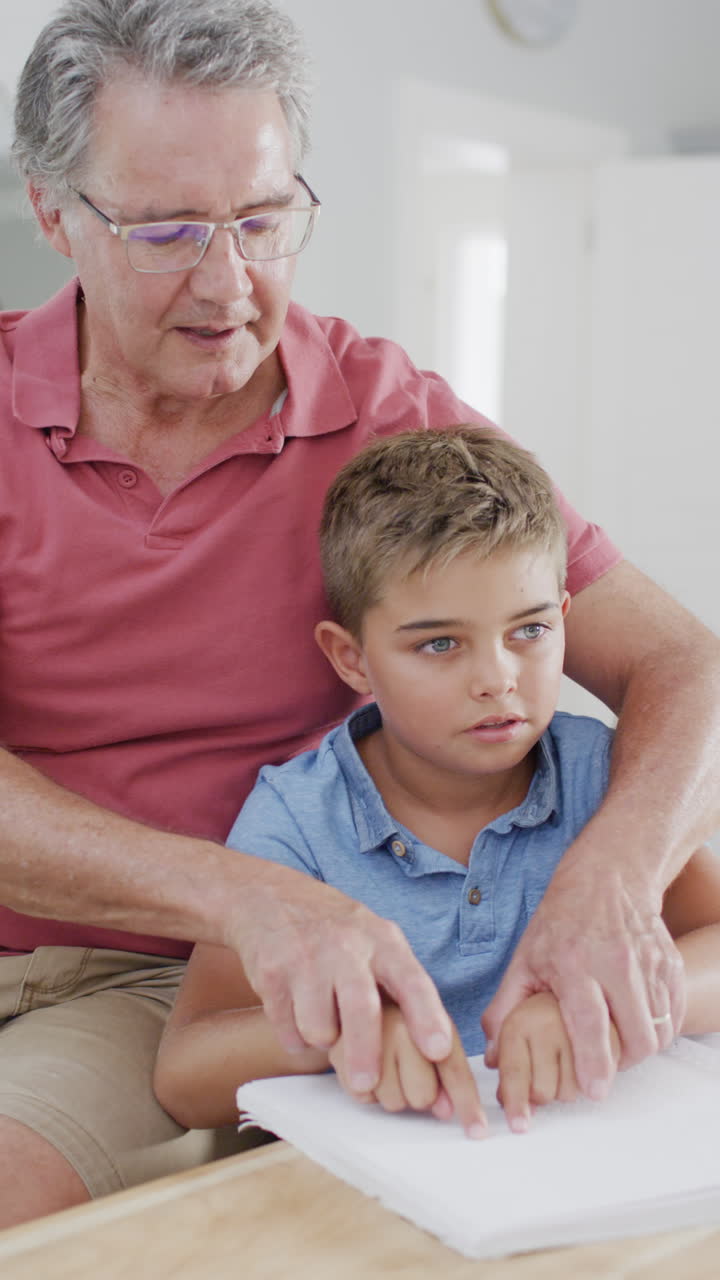 Vertical video of caucasian father and son sitting at table and reading braille, slow motion
