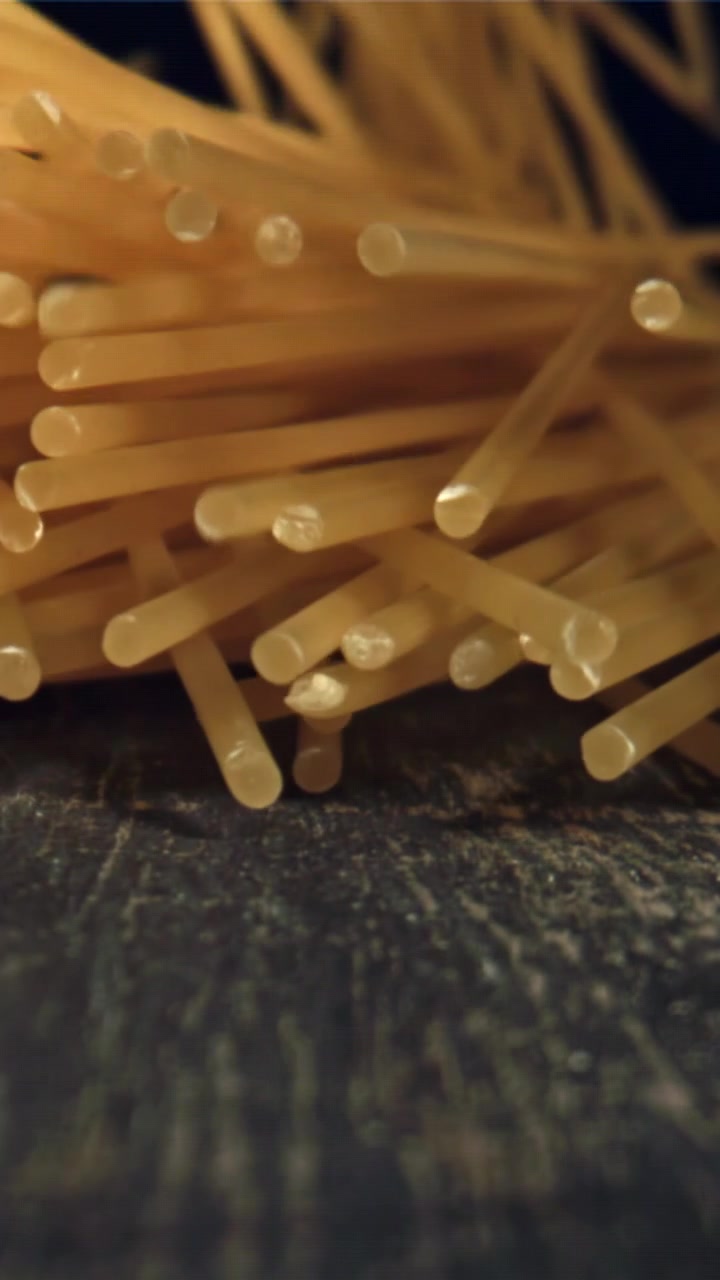 Spaghetti crudi che cadono al rallentatore su una superficie scura.