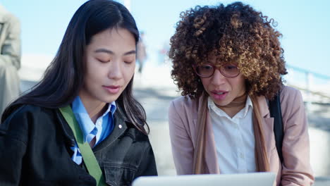 young female coworkers using laptop and speaking outdoors