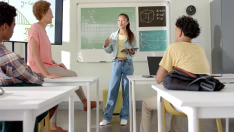 holding tablet and speaking to classmates, teenage girl presenting in high school classroom