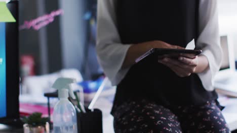 Mid-section-of-woman-cleaning-digital-tablet-with-tissue-at-modern-office